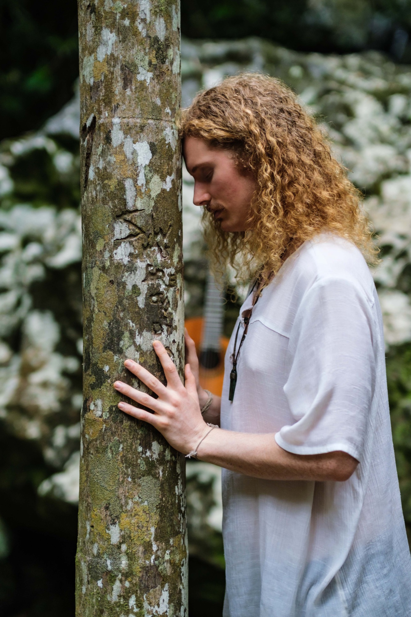 Alexander in profile, with his head and hands resting against a rainforest tree.