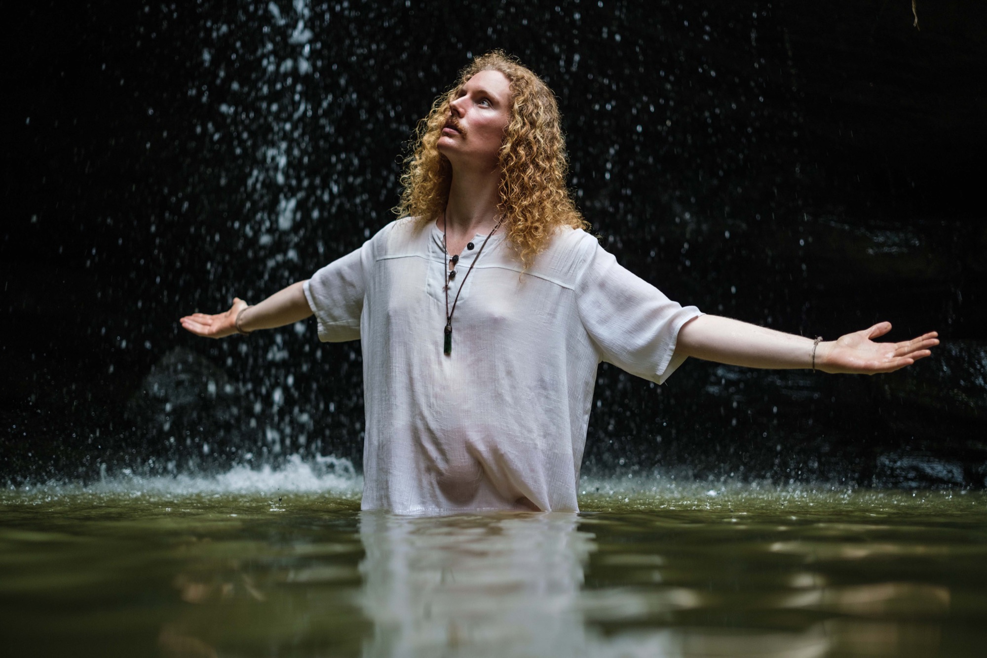 Alexander standing in a waterfall pool with his arms open.